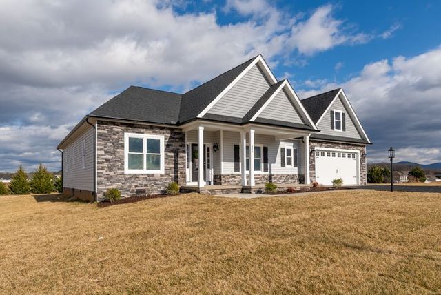 House with gray stone siding, white trim, and a two-car garage under a blue sky with fluffy clouds.