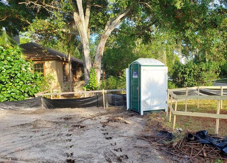 A brown portable toilet is sitting in front of a house under construction.