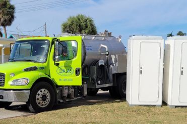 A green truck is parked next to a row of portable toilets.