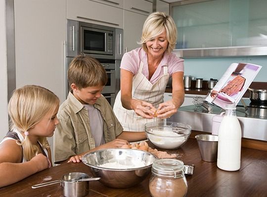A woman and two children are preparing food in a kitchen.