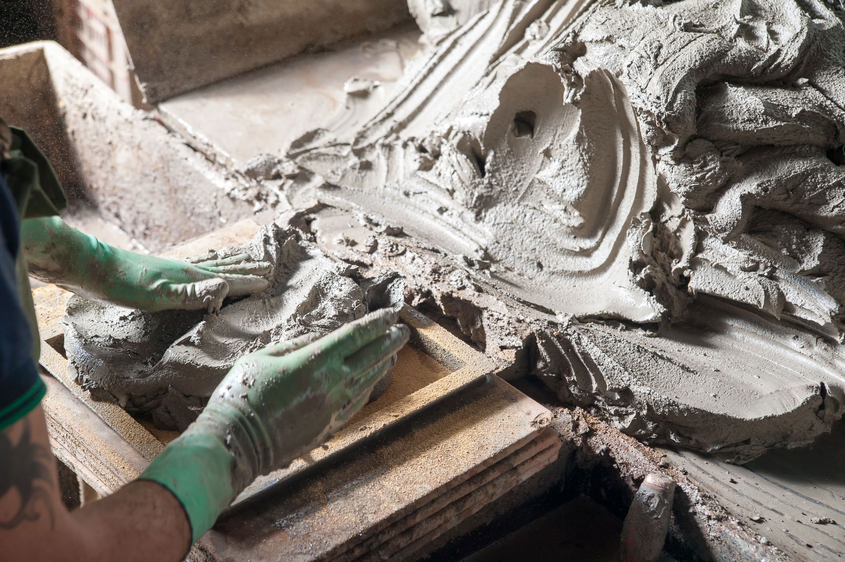 A person wearing green gloves is working on a piece of concrete.