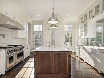 White kitchen with a dark wood island, stainless steel appliances, and pendant lights. Sunlight streams through windows.