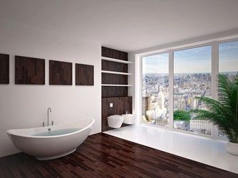 Bathroom with dark wood floors, white walls, and a city view through large windows. Contains a tub, toilet, and shelves.