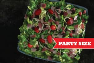 A salad with lettuce , tomatoes , ham and olives on a plate.