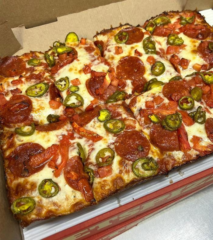 A pepperoni pizza with tomatoes and jalapenos in a box