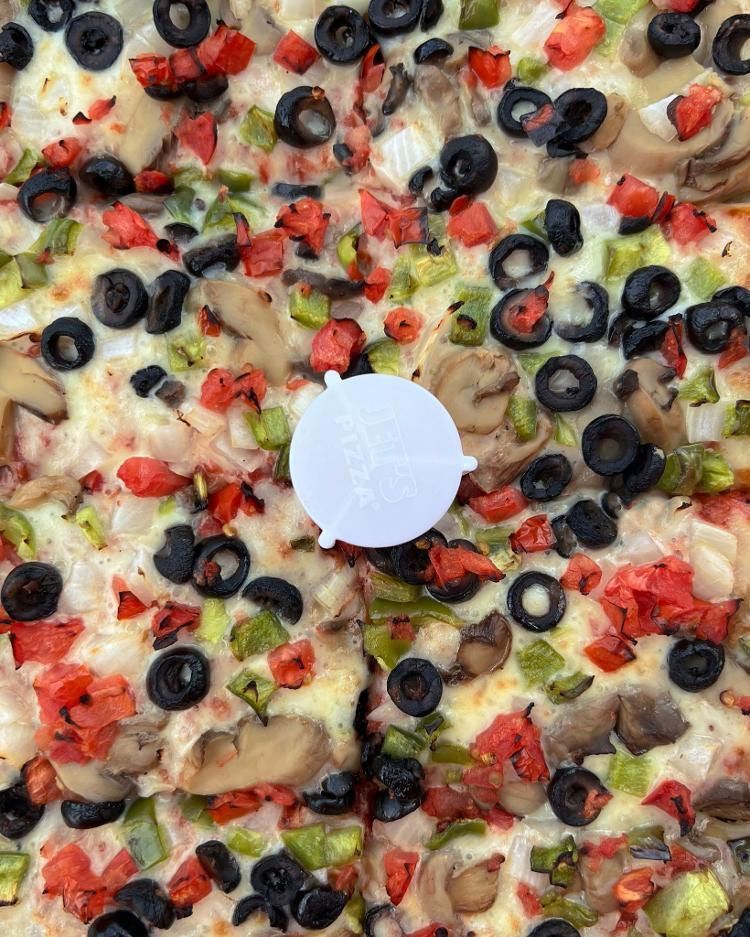 A pizza with mushrooms , olives , peppers , and cheese is sitting on a table.