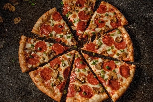 A pizza with pepperoni , mushrooms , green peppers and cheese is cut into slices on a table.