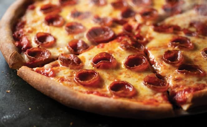 A pepperoni pizza with a slice taken out of it on a table.