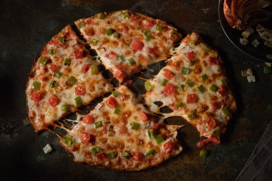 A pizza with tomatoes , green peppers and cheese is being cut into slices.