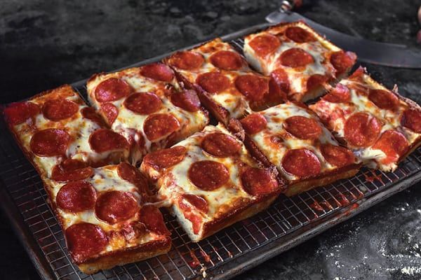 A pepperoni pizza is being cut into squares on a wire rack.
