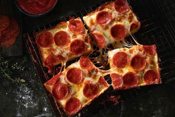 Four slices of pepperoni pizza are sitting on a cooling rack.