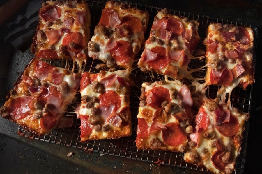 A bunch of square pizzas are sitting on a wire rack.