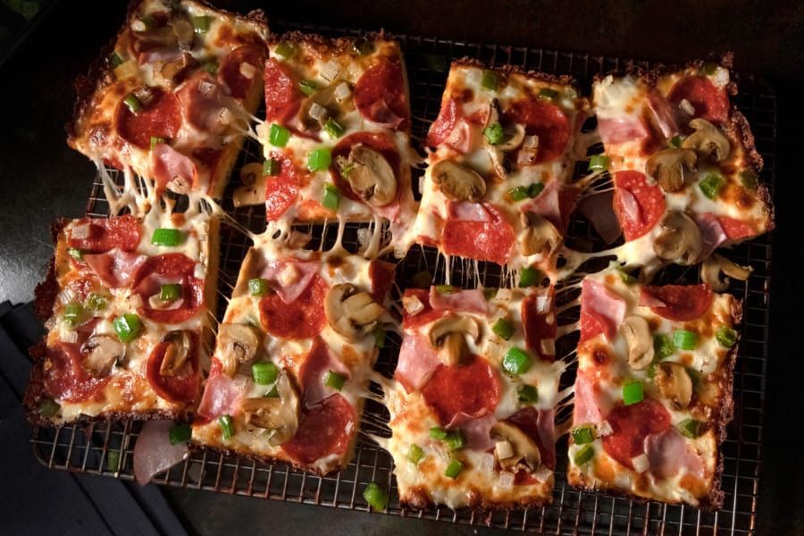 A pizza with pepperoni , mushrooms , green peppers and cheese is sitting on a cooling rack.