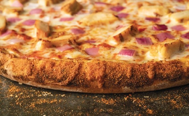 A close up of a pizza with cajun and onions on a table.