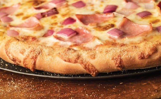 A pizza with garlic and onions is on a pan on a table.