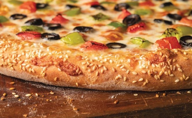 A pizza with sesame seeds on it is sitting on a wooden cutting board.