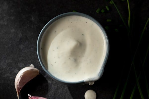 A bowl of ranch dressing next to garlic and chives