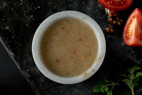 A bowl of Italian dressing with tomatoes in the background