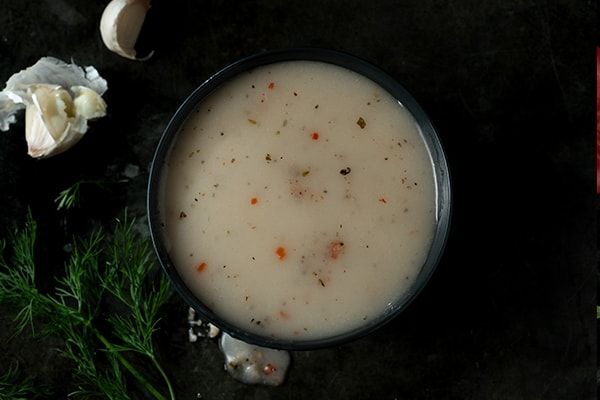 A bowl of Greek dip with garlic and dill on a table.