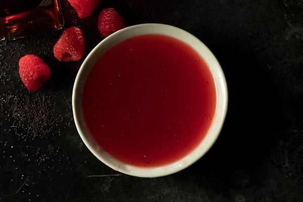 A bowl of red dip next to raspberries on a table.