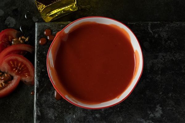 A bowl of catalina dip is sitting on a table next to tomatoes and olive oil.