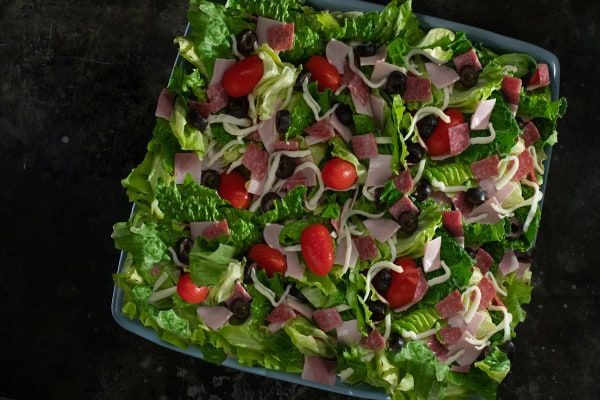 A salad with lettuce , tomatoes , olives and ham on a plate.