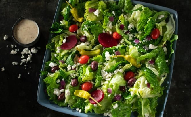 A salad with lettuce , tomatoes , olives , peppers and feta cheese on a plate.
