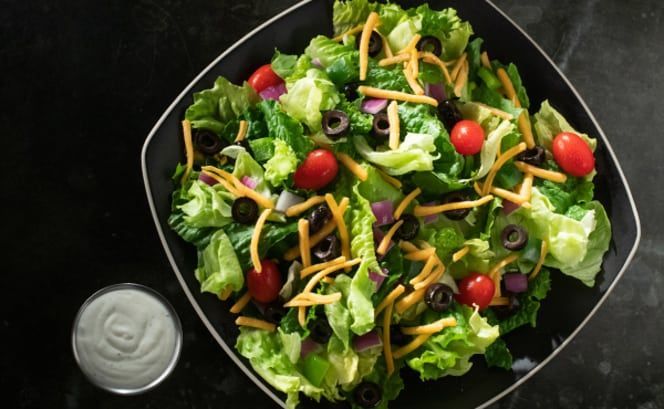 A salad with lettuce , tomatoes , olives , cheese and ranch dressing in a bowl.