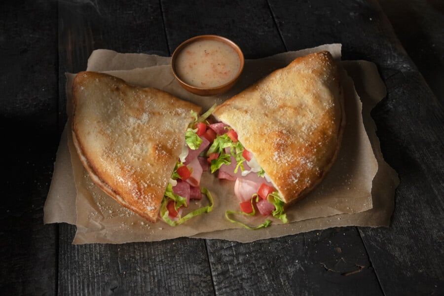 A close up of a sandwich on a wooden table with a dipping sauce.