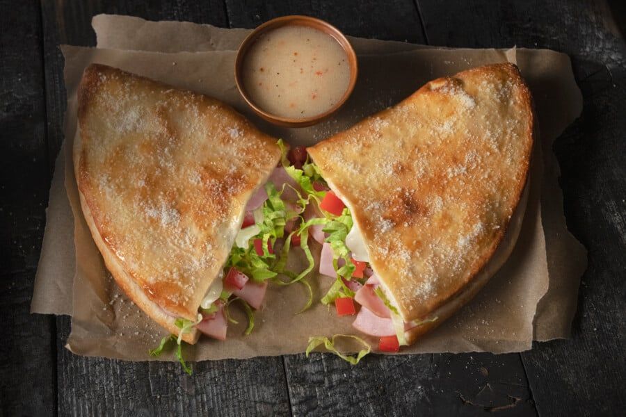 A sandwich is cut in half and sitting on a piece of paper on a wooden table.