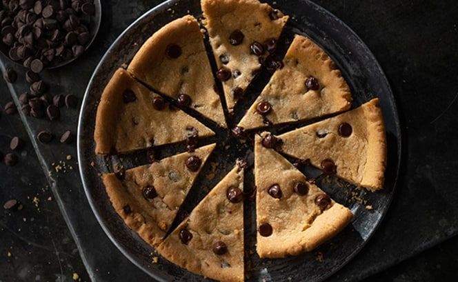 A chocolate chip cookie pie is cut into slices on a plate.