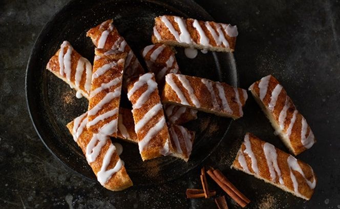 A plate of cinnamon sticks with icing and cinnamon sticks on a table.
