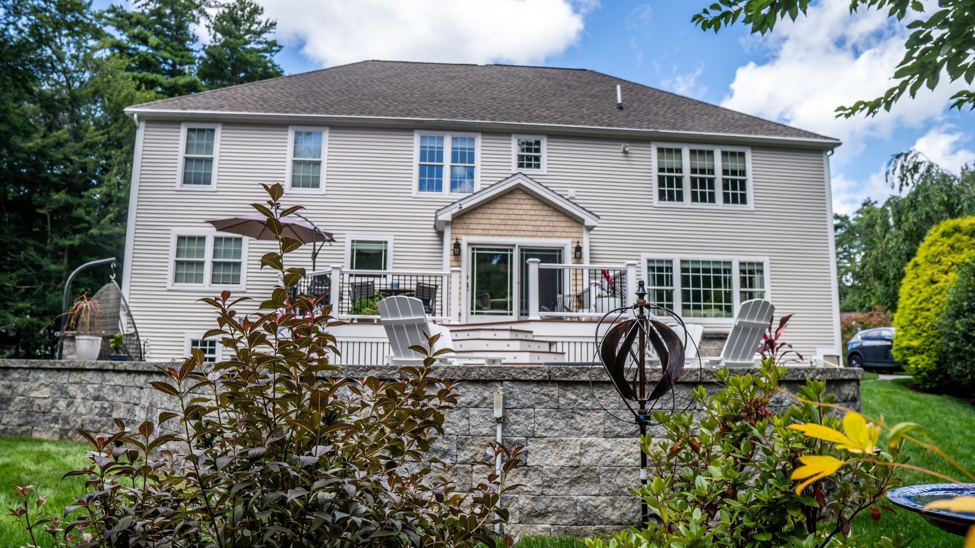 The back of a large house with a large deck and a bird bath in front of it.