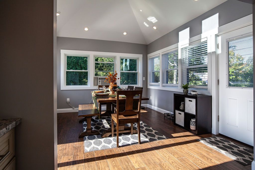 A dining room with a table and chairs and lots of windows.
