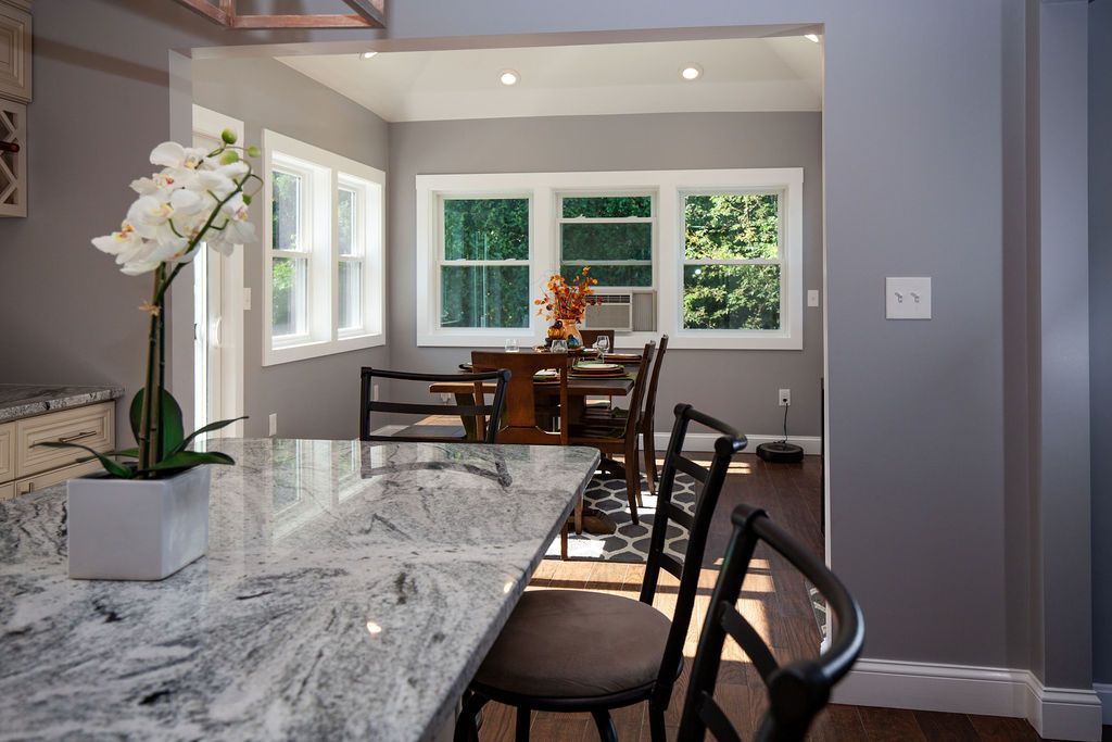 A kitchen with a granite counter top and a dining room in the background.