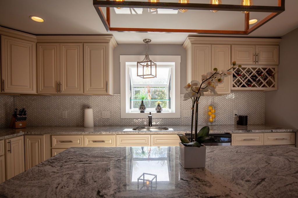 A kitchen with white cabinets , granite counter tops , a sink , and a window.