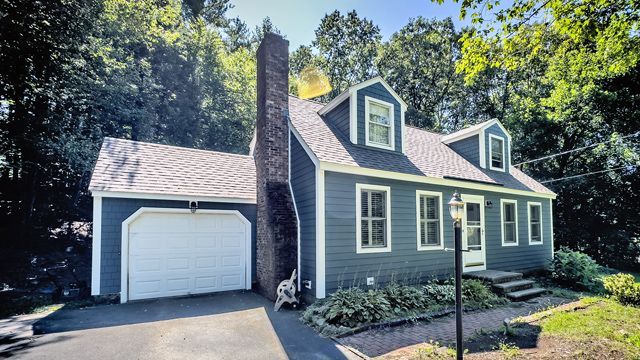 A house with a garage and a chimney is surrounded by trees.