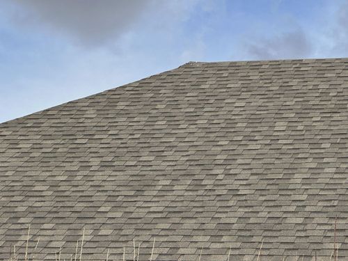 Close-up of a gray shingled roof against a blue sky with clouds