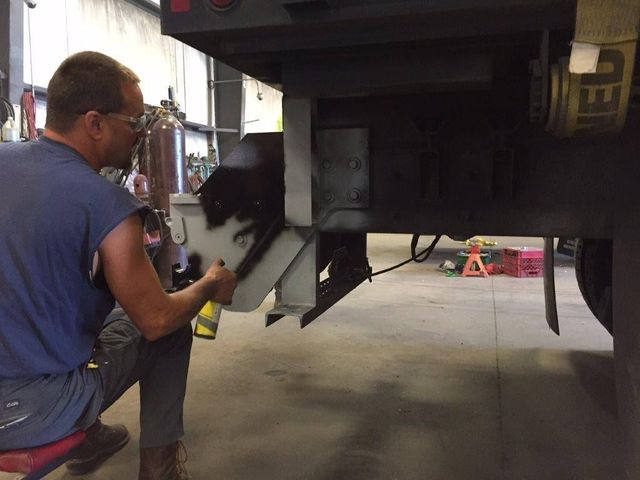 Mechanic inspecting the underside of a vehicle in a garage, holding a tool near the rear wheel.