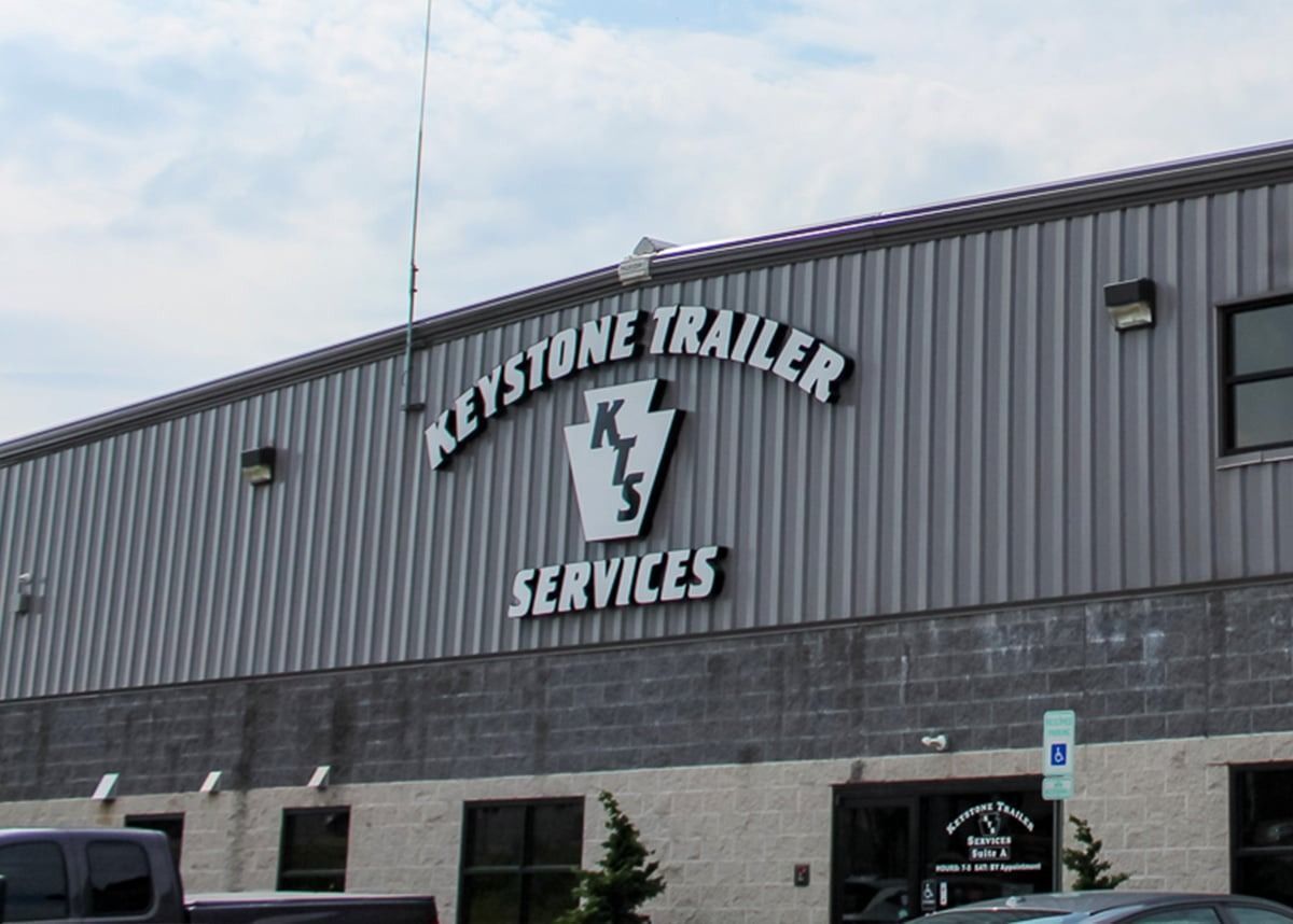 Exterior of the Keystone Trailer Services building with a prominent sign and a gray metal facade above a concrete base.