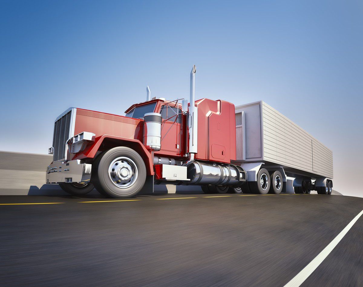 A red semi-truck with a white trailer drives down a paved highway under a clear blue sky.