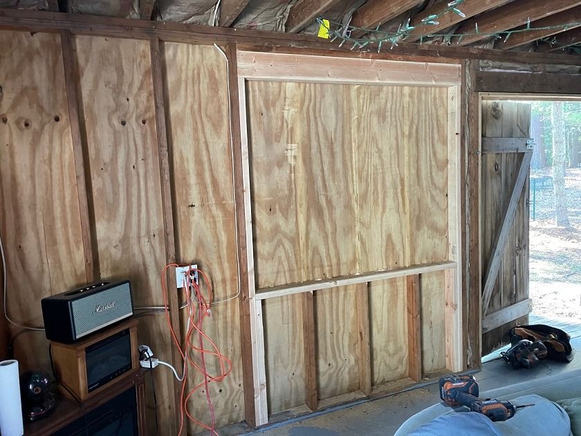 Unfinished wooden shed interior with exposed studs, hanging wires, and a workbench near an open door.