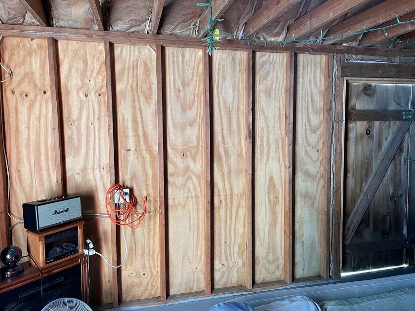 Interior of unfinished shed wall with exposed studs, a small shelf, and a door on the right.
