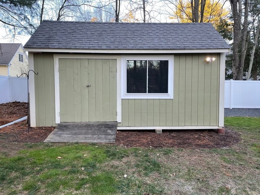 Small green shed with white trim and a window in a backyard