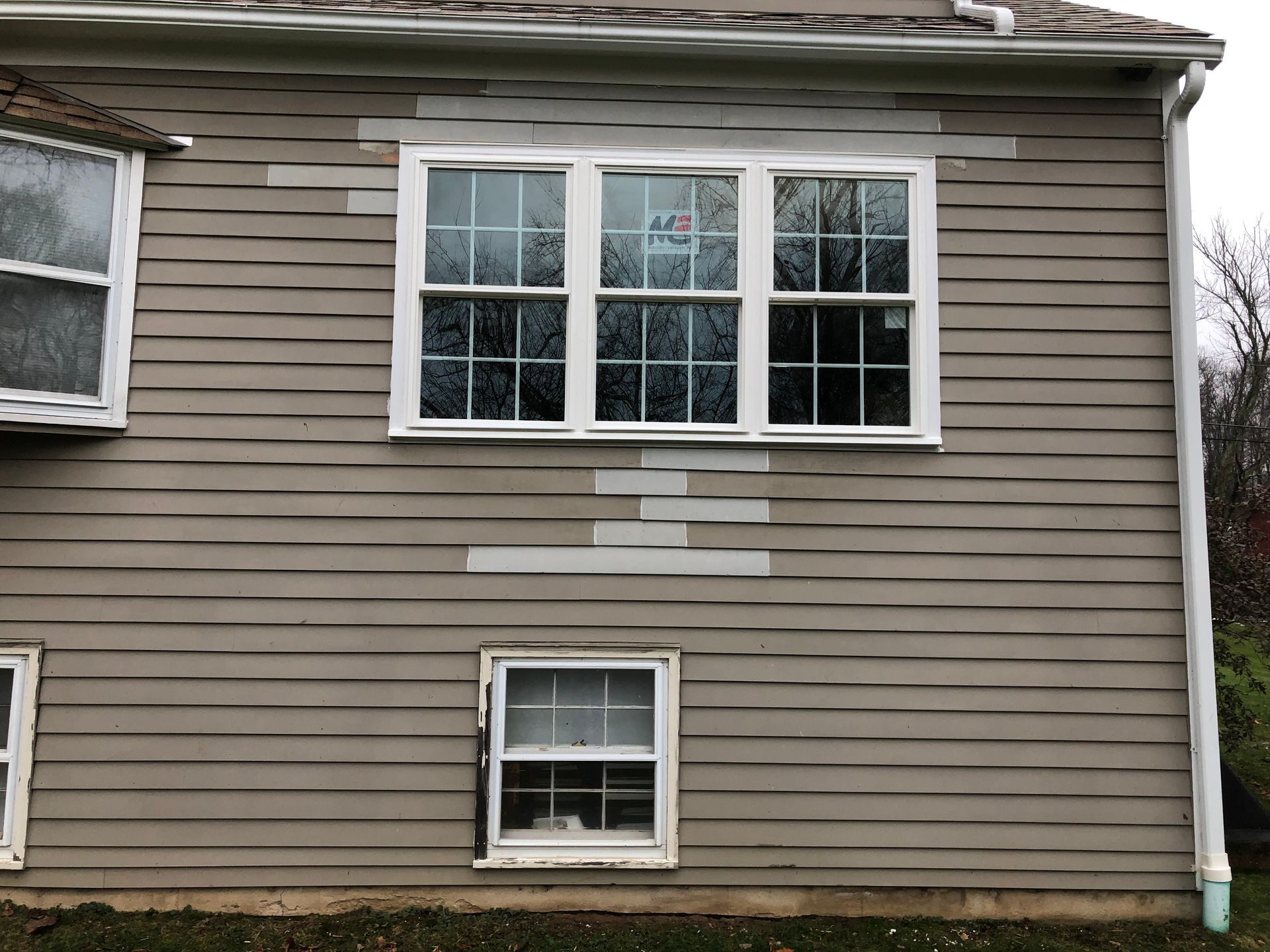Exterior of beige house with white-trimmed windows and patchy paint repairs
