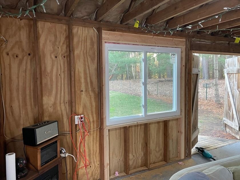 Unfinished wooden room with a window, exposed wiring, and a small TV on a stand near the wall.