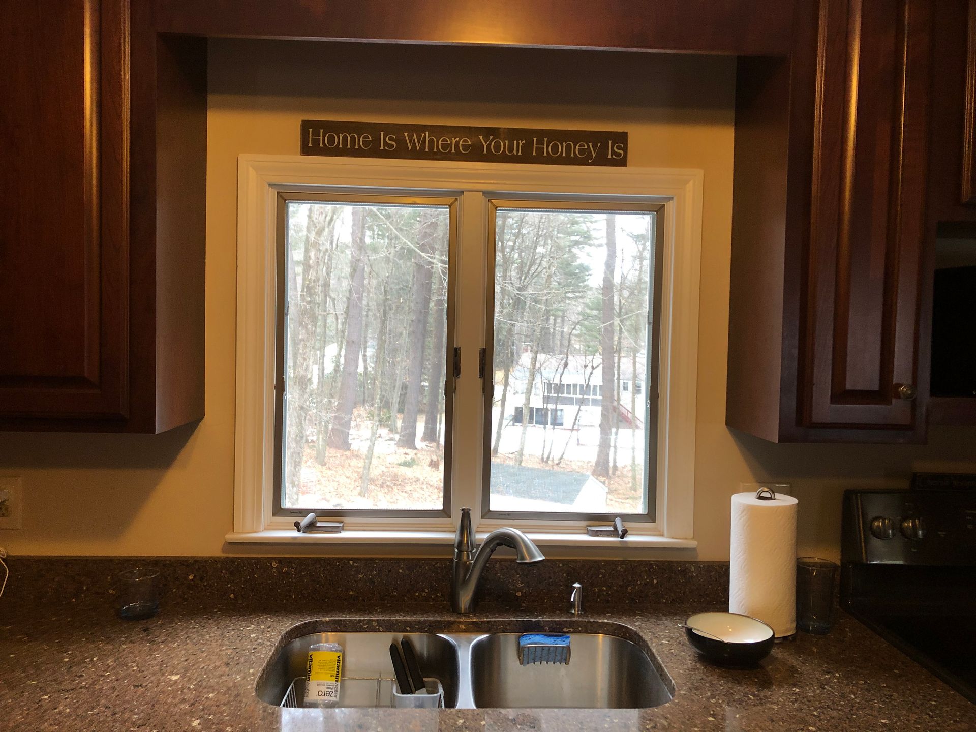 Kitchen sink beneath a window, with dark wood cabinets and a paper towel holder on the counter.