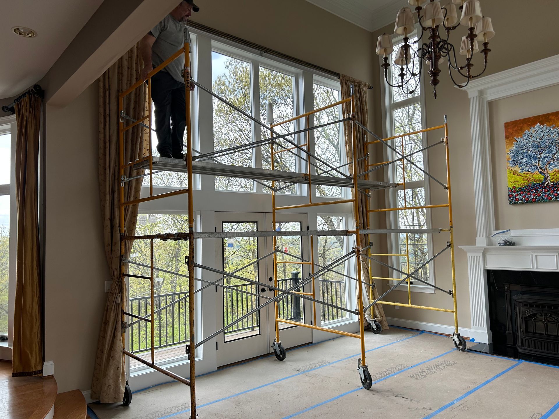 Scaffolding inside a bright room with tall windows, chandelier, and fireplace during interior work