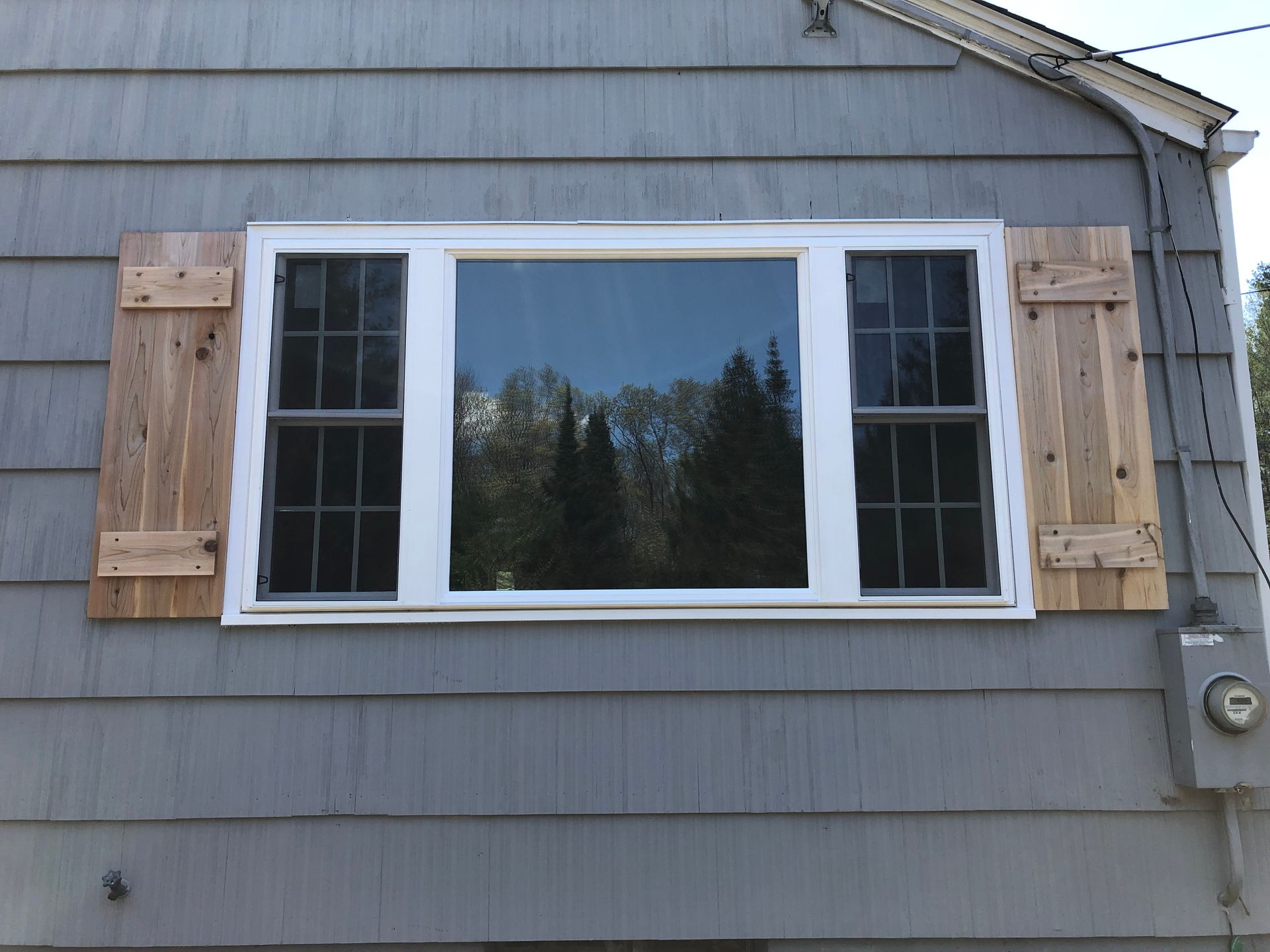 House exterior with a white-framed window and wooden shutters on gray siding