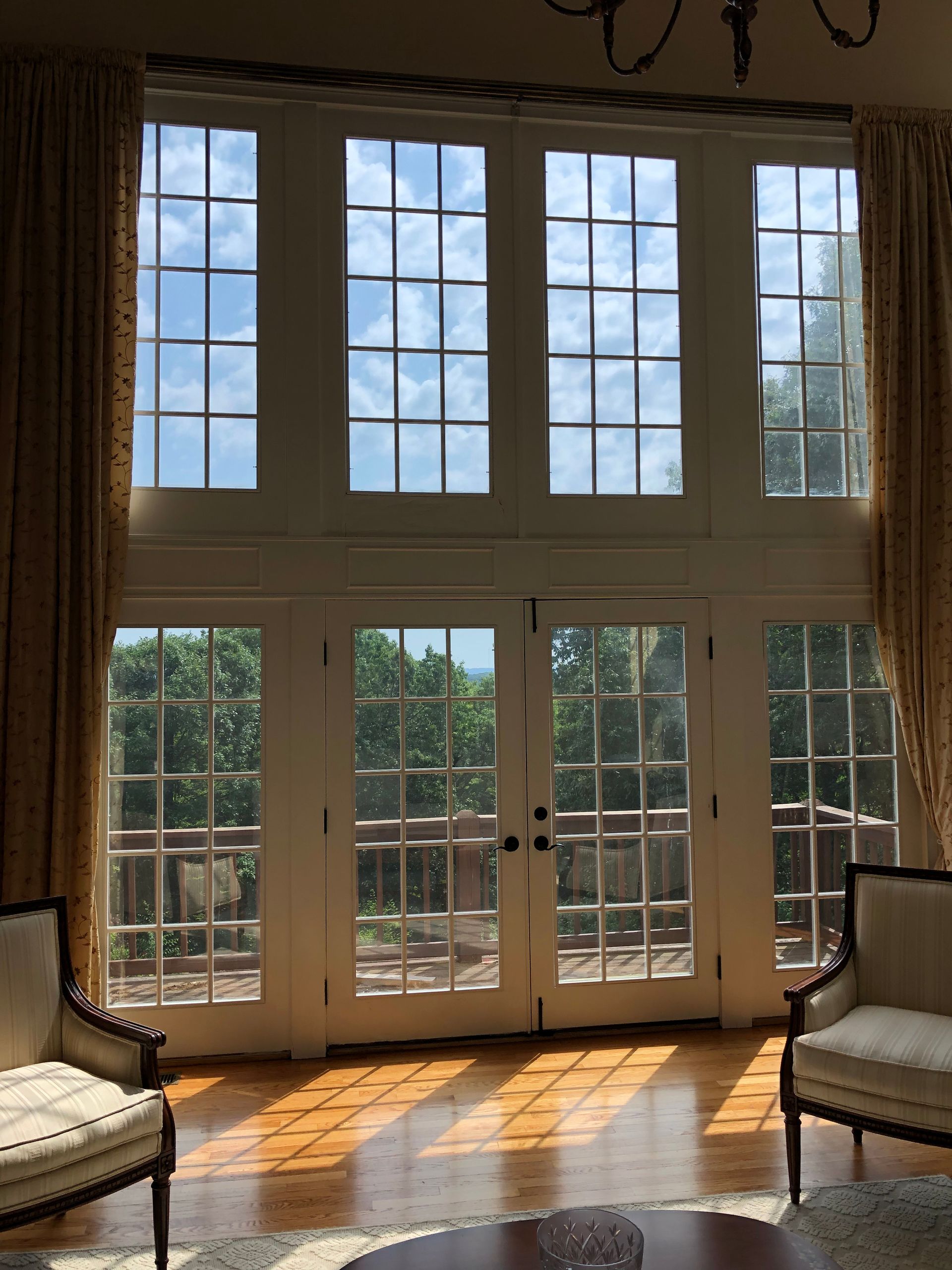 Tall French doors and windows in a sunlit room, with chairs on either side and light on the wooden floor